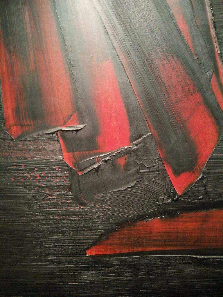 Traces de peinture noire sur un fond rouge qui apparaît sous les traces noires raclées