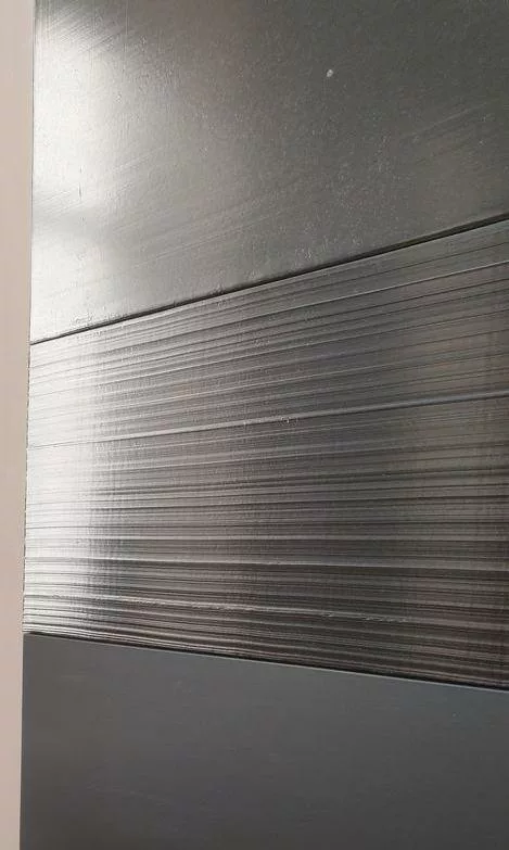 Photo prise en biais d'un tableau fait de bandes noires. L'une est lisse et brillante, en-dessous, l'autre est striée et brillante, la dernière est lisse et matte.