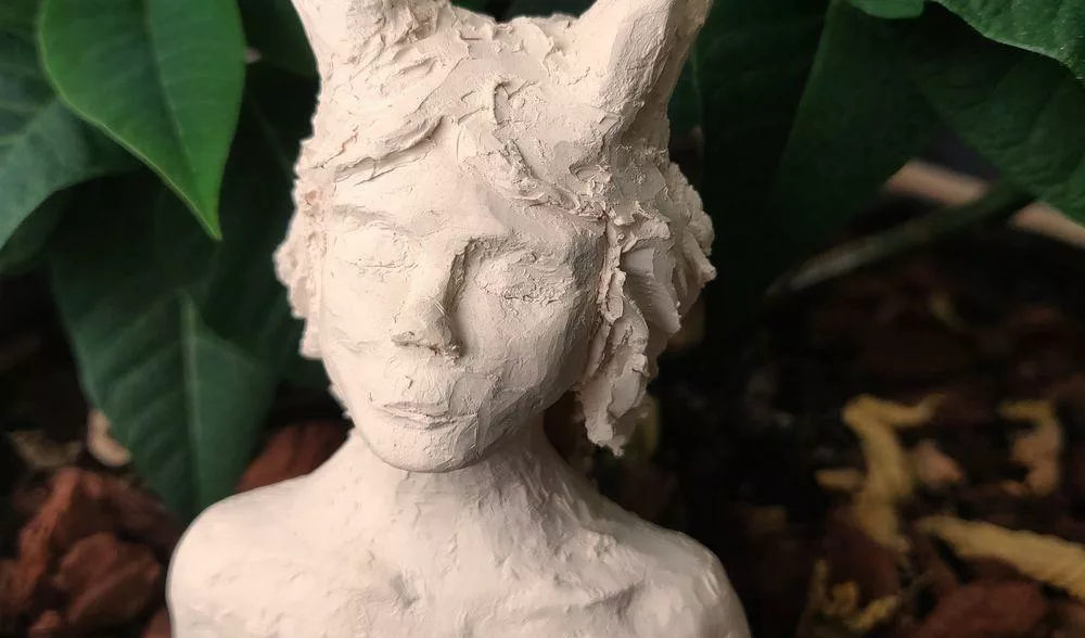 Gros plan sur une sculpture en argile blanche représentant un buste d'une femme aux paupières close et avec des bois (de cerf)