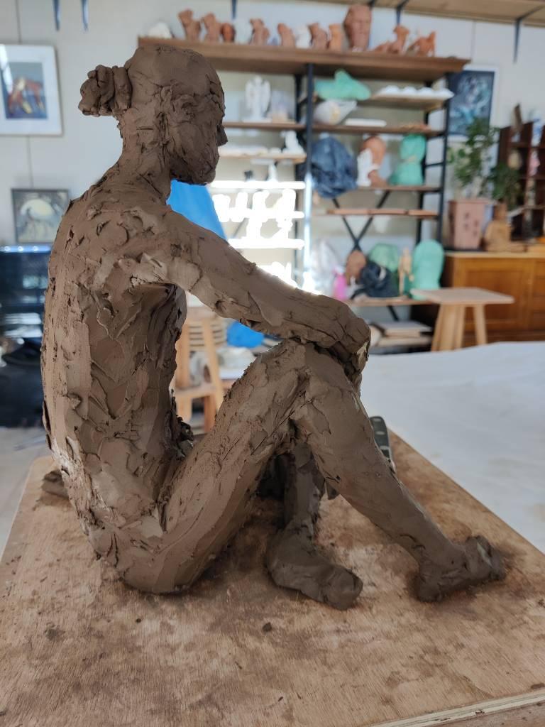 Sculpture en terre en cours de réalisation - les formes sont assez définies mais avec encore beaucoup de choses à affiner : un homme assis au sol de profil, un genou replié et son coude posé dessus
