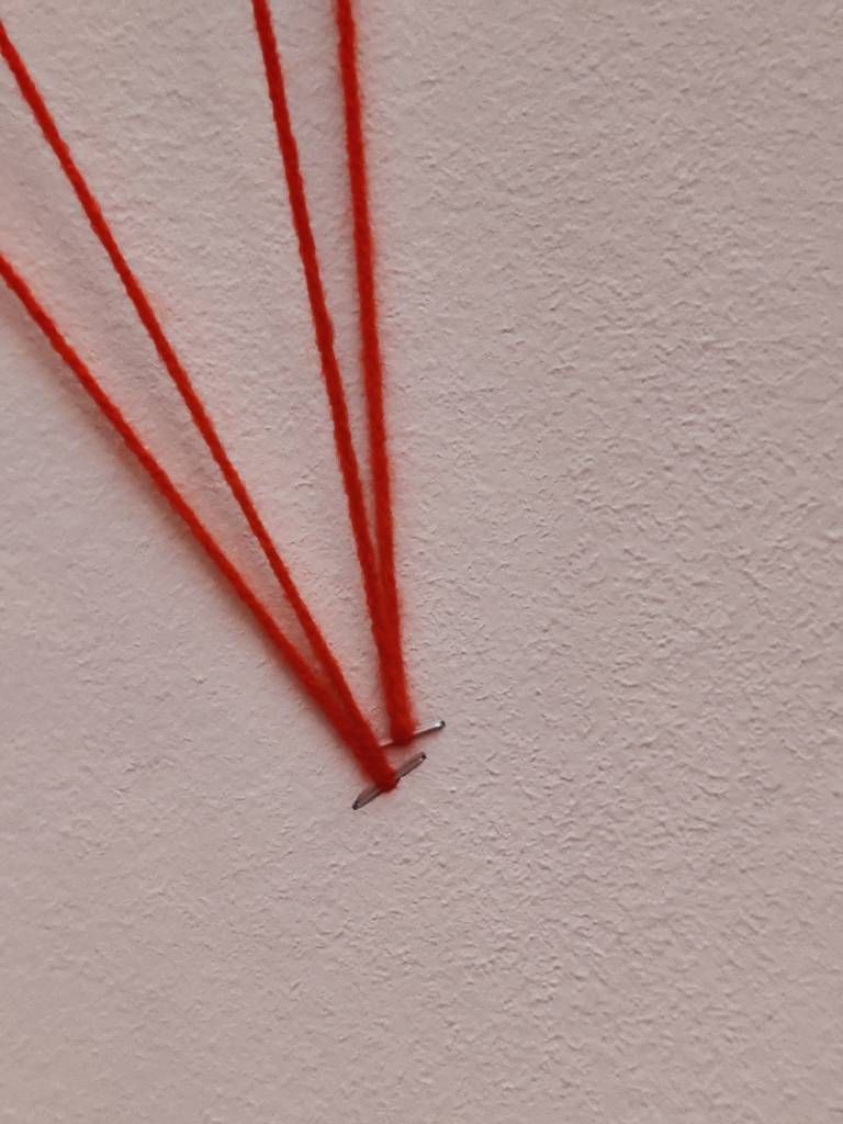 Deux fils rouges accrochés à un mur avec des agrafes qui leurs permettent de repartir formant ainsi un triangle