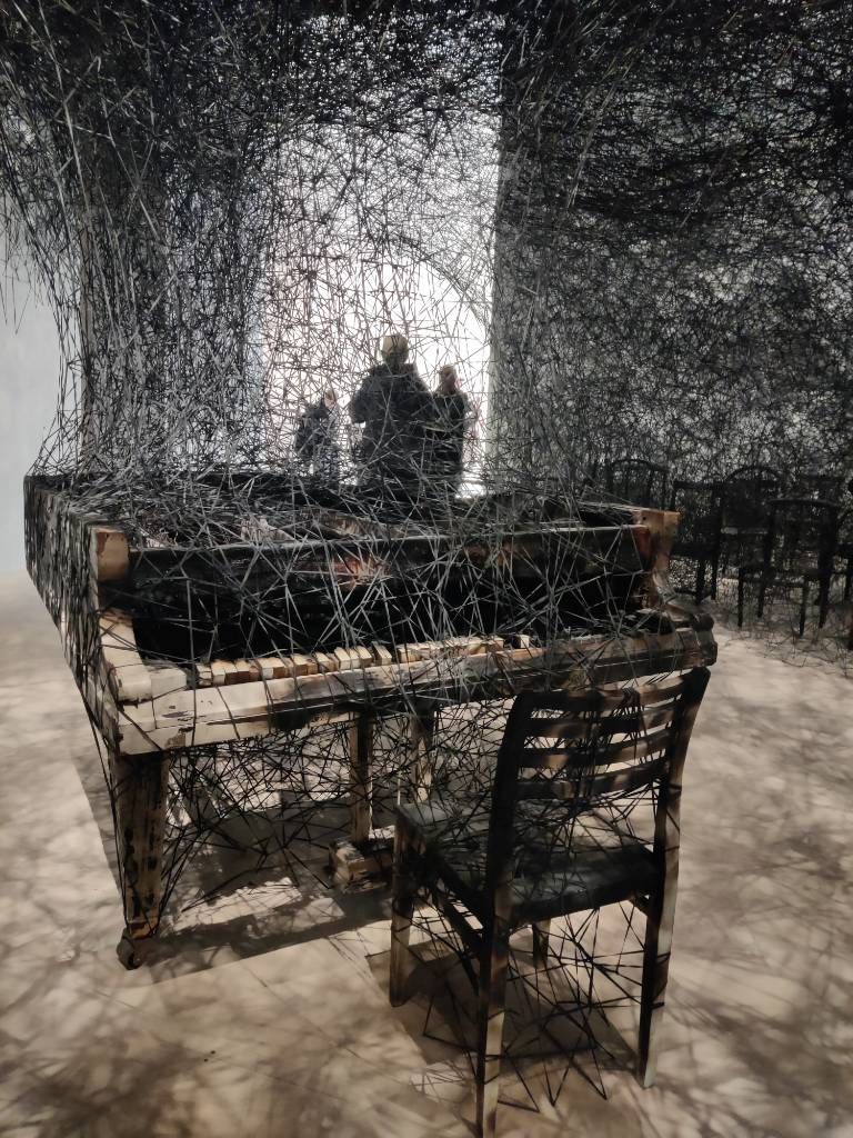 Un piano brûlé et un chaise pris dans un enchevêtrement de fils noirs
