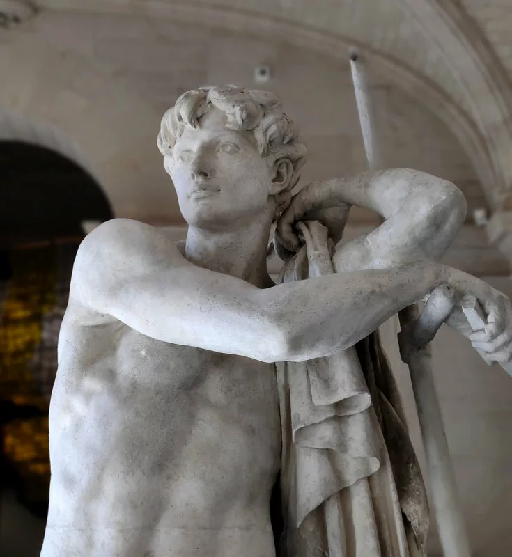 Haut d'une sculpture représentant un homme torse nu, appuyé sur sa faux