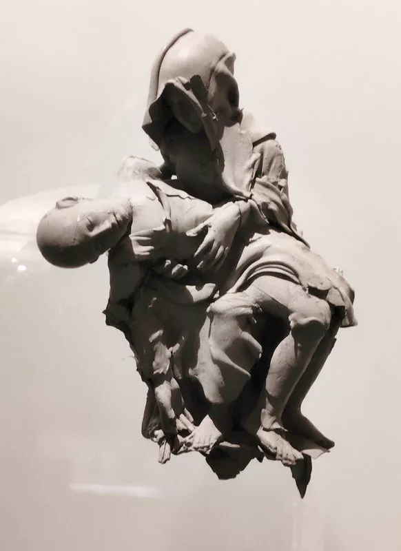 Sculpture où un personnage en tient un autre sur ses genoux. Le premier est cagoulé, le second est chauve