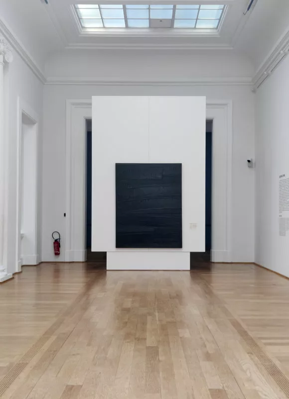 Dans une pièce blanche et lumineuse, un tableau noir où seuls les reflets de lumière se distinguent