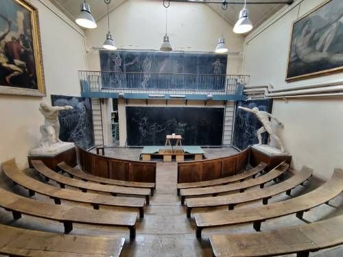 Petit amphithéâtre avec des grands tableaux aux murs, des sculptures grandeur nature, plusieurs tableaux noirs avec des dessins à la craie