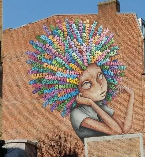 Sur toute la hauteur d'une façade d'immeuble, le buste d'une femme stylisé dont les cheveux évoquent une coupe afro mais dont les mèches sont des mots (Roubaix, Ch'nord, théatre, usine, textile, piscine, joie, etc.)