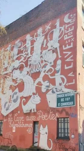 Sur le mur d'un immeuble, une fresque représentant des personnages rigolos, des animaux, etc. "La cave aux poètes" + un écriteau "Syndicat autonome des VRP et commerciaux"