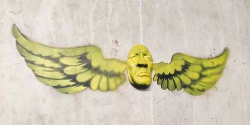 Un visage collé (en relief) faisant la moue entouré de deux ailes déployées