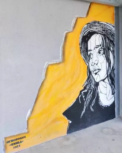 Graff occupant toute la hauteur d'un mur représentant le buste d'une femme avec un chapeau, en noir et blanc sur un fond jaune très lumineux "Ouroboros "Embla" 2021"