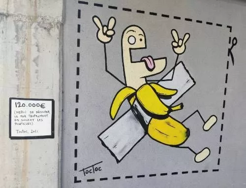 Peinture murale d'une banane humanisée et rigolote dans le style habituel de TocToc, scotchée au mur, encadrée de pointillés avec un symbole de ciseaux Sur la gauche, un écriteau : "120.000€ (Merci de découper le mur proprement en suivant les pointillés). TocToc, 2021"