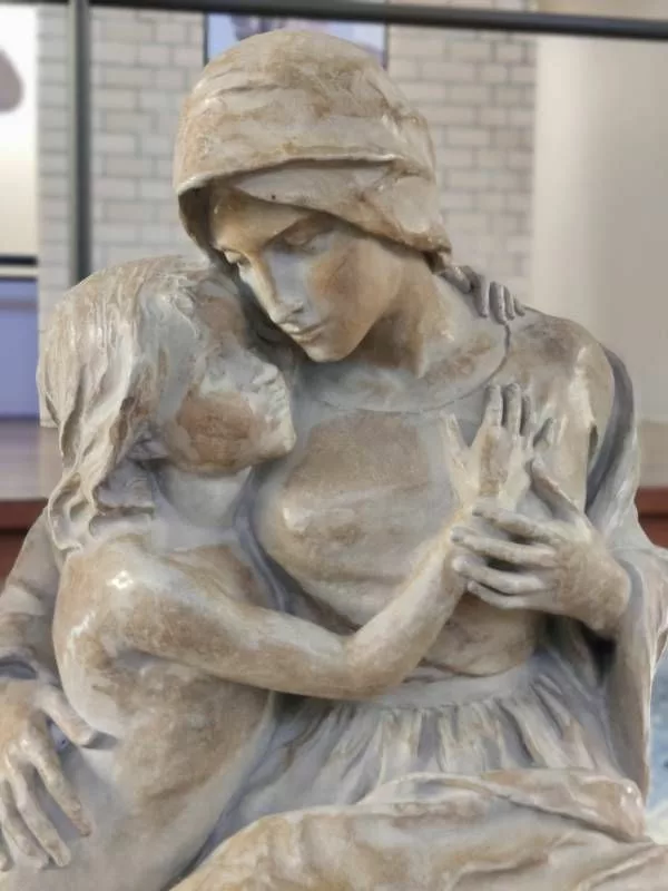 Sculpture représentant une femme penchée vers un enfant qui semble s'accrocher à elle