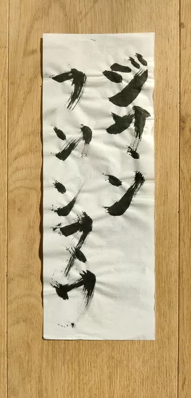 Sur un papier de calligraphie japonaise qui a un peu gondolé, traces d'encre noires faisant, normalement, penser à du japonais