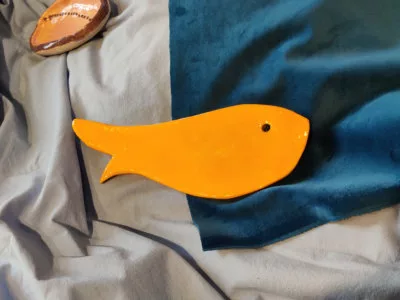 Adorable petit poisson très stylisé en céramique posé sur un tissu