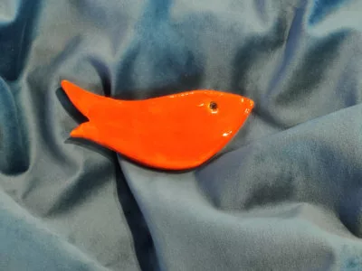 Adorable petit poisson très stylisé en céramique posé sur un tissu