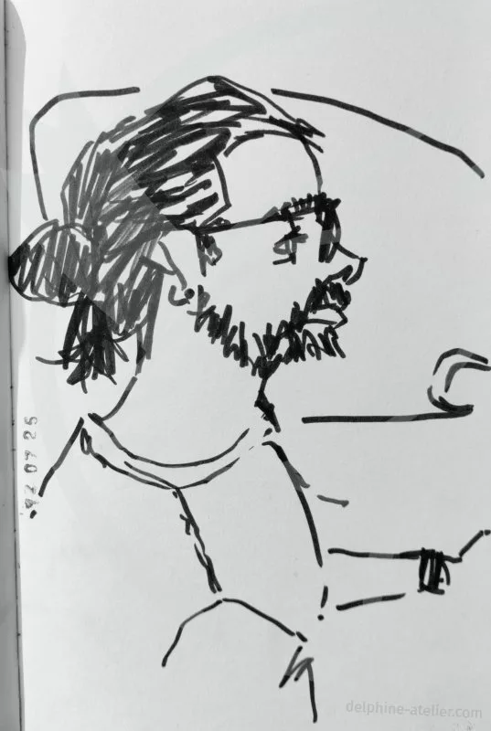 Dessin au feutre noir d'un homme barbu, cheveux en chignon de profil. On devine une fenêtre de voiture derrière lui. Un tampon indique "12 07 25"