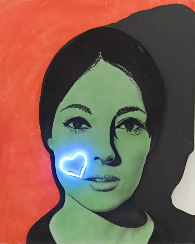 Tableau avec la photographie d'une femme en deux couleurs (noir et vert) sur fond orange et avec son ombre. Elle a, sur la joue, un cœur en néon bleu