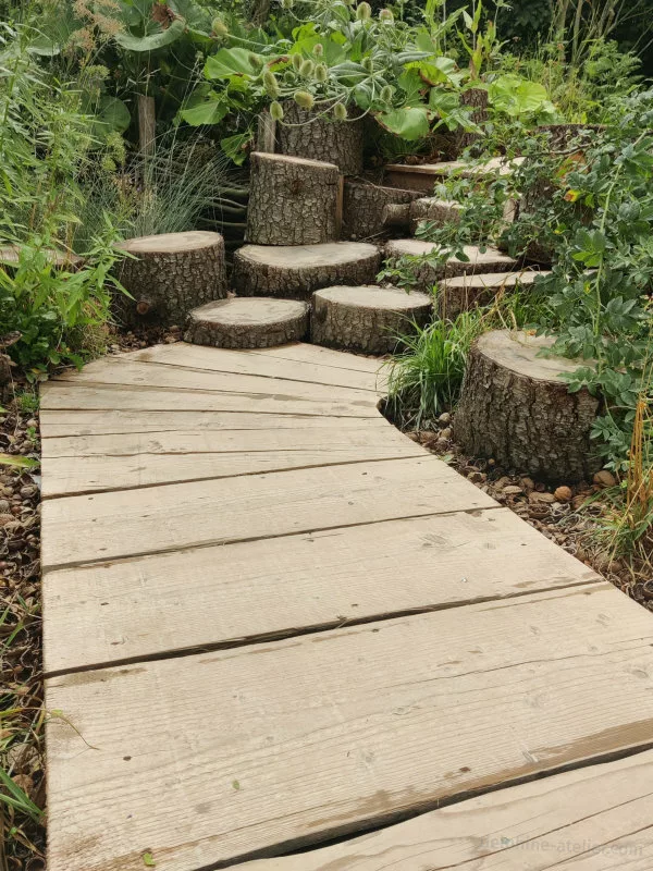 Un chemin fait de planches de bois puis de souches de tailles différentes pour faire un escalier