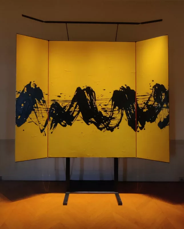 Un tableau abstrait en triptyque où une ligne vive noire traverse un fond jaune. Les panneaux sont séparés par une rayure rouge