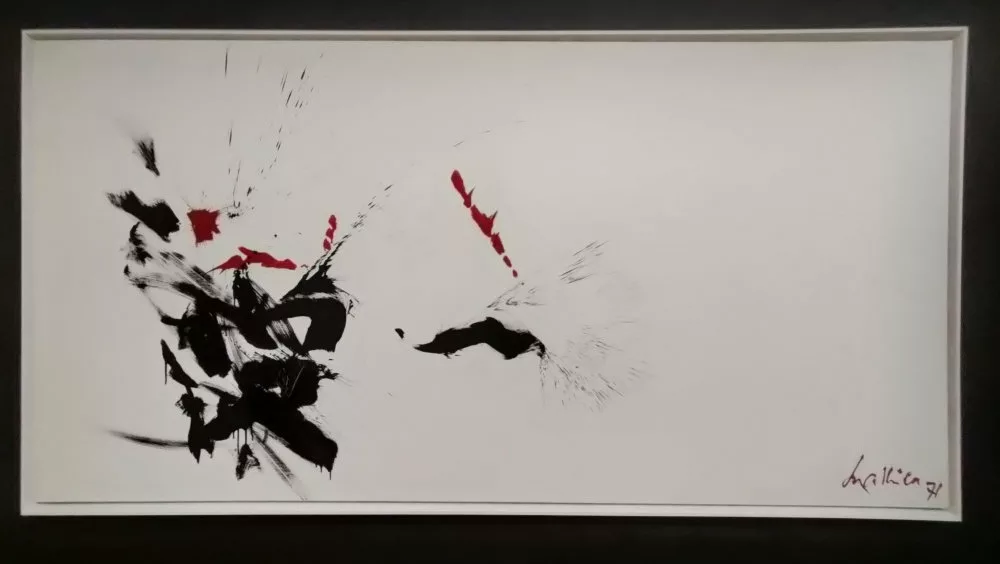Un tableau abstrait avec traces dynamiques de noir et de rouge sur un fond blanc ; seule la moitié gauche du tableau est occupée