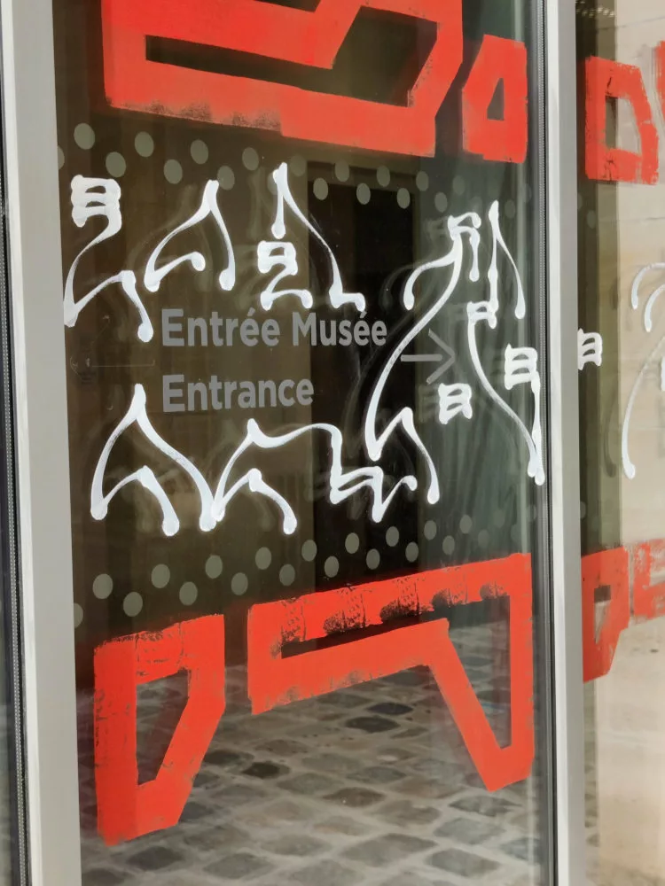 Sur une vitre : "Entrée Musée Entrance" avec des éléments graphiques