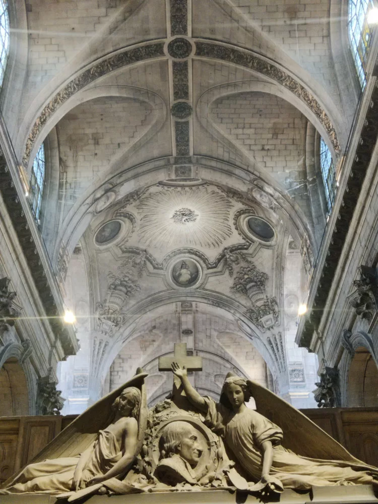 Deux anges sculptés autour d'un médaillon d'un homme de profil et, dans le fond, le plafond sculpté d'une église