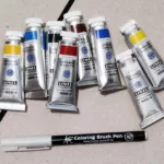 Six tubes de gouache Linel (deux bleus, deux rouges, deux jaunes, un noir, un blanc) et un feutre "Coloring Brush Pen" gris Koi