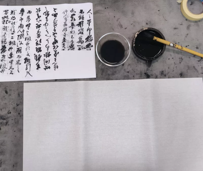 Une table de travail avec des idéogrammes chinois dans différents sens de lecture, de l'encre et un pinceau, une feuille blanche