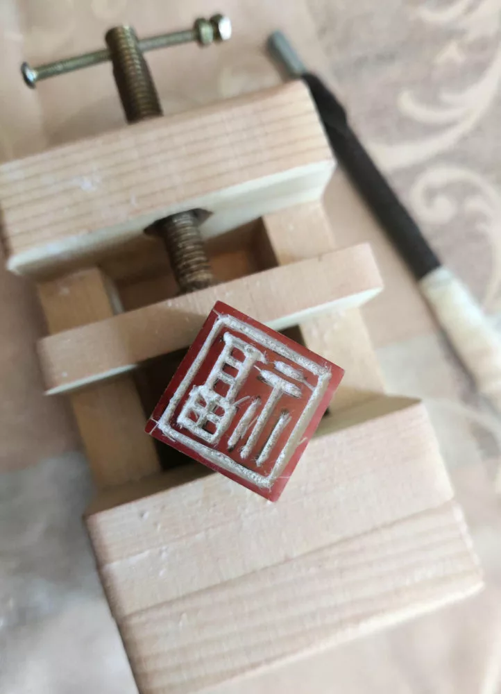 Une pierre à sceau prise dans un petit étau en bois