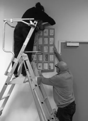 Deux personnes dont une sur une échelle en train d'accrocher des tableaux