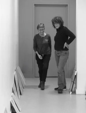 Deux personnes dans un couloir avec des tableaux au sol appuyés sur le mur