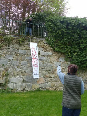 Deux personnes en train d'accrocher une grande affiche verticale sur un mur extérieur