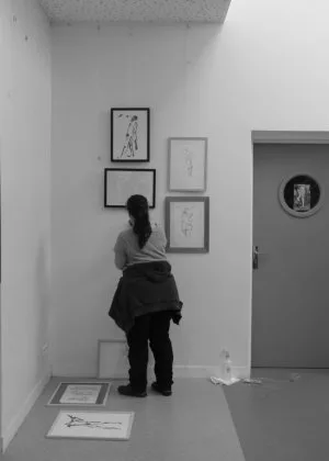 Une personne en train de réfléchir à un accrochage en cours (tableaux au mur et au sol)