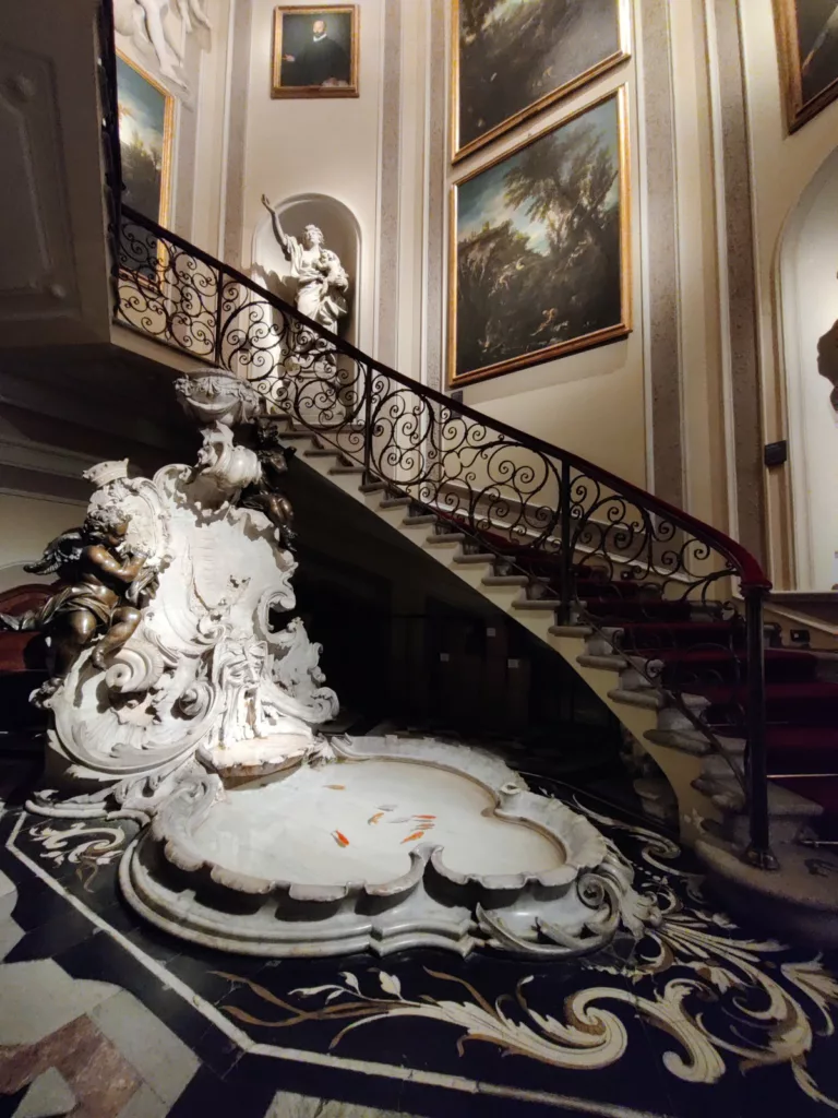 Escalier avec une fontaine à sa base et des tableaux et sculptures le long de la montée