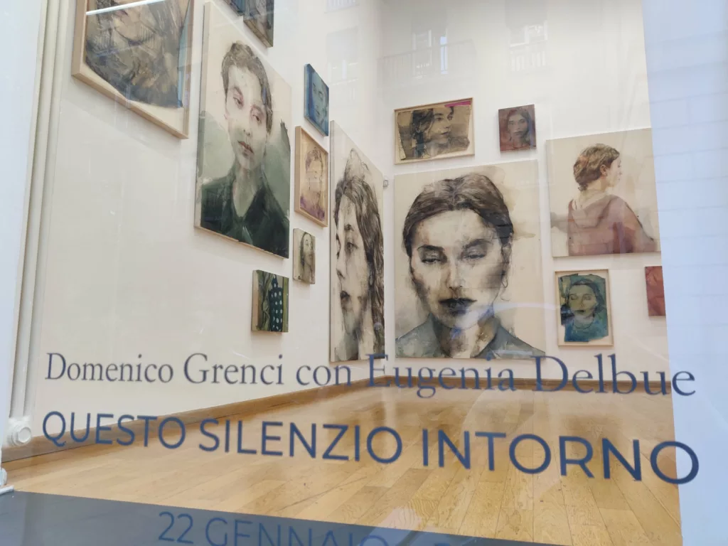 Vitrine d'une galerie d'art où on voit des portraits très délicats. Sur la vitre : "Domenico Grenci con Eugenia Delbue - Questo silenzio intorno - 22 gennaio... [suite non visible]