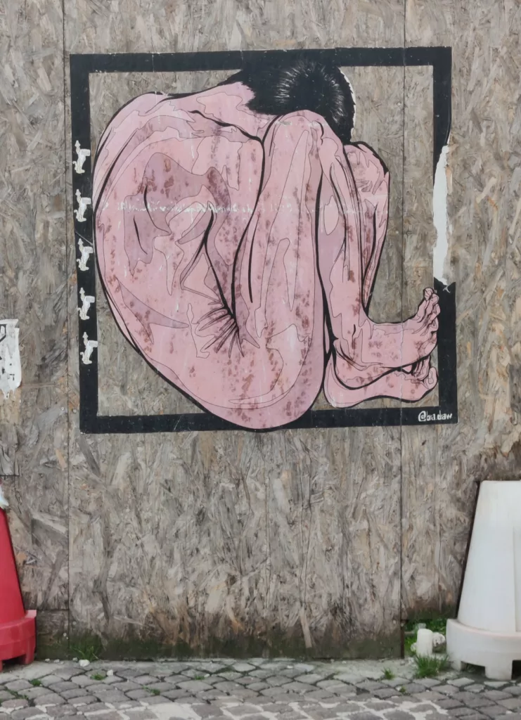 Œuvre de street art sur une palissade représentant un homme recroquevillé dans un carré