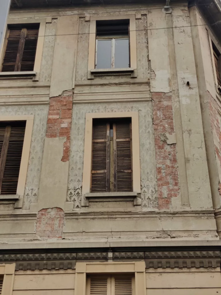 Un immeuble dont des morceaux de décors manquent laissant apparaître la brique rouge