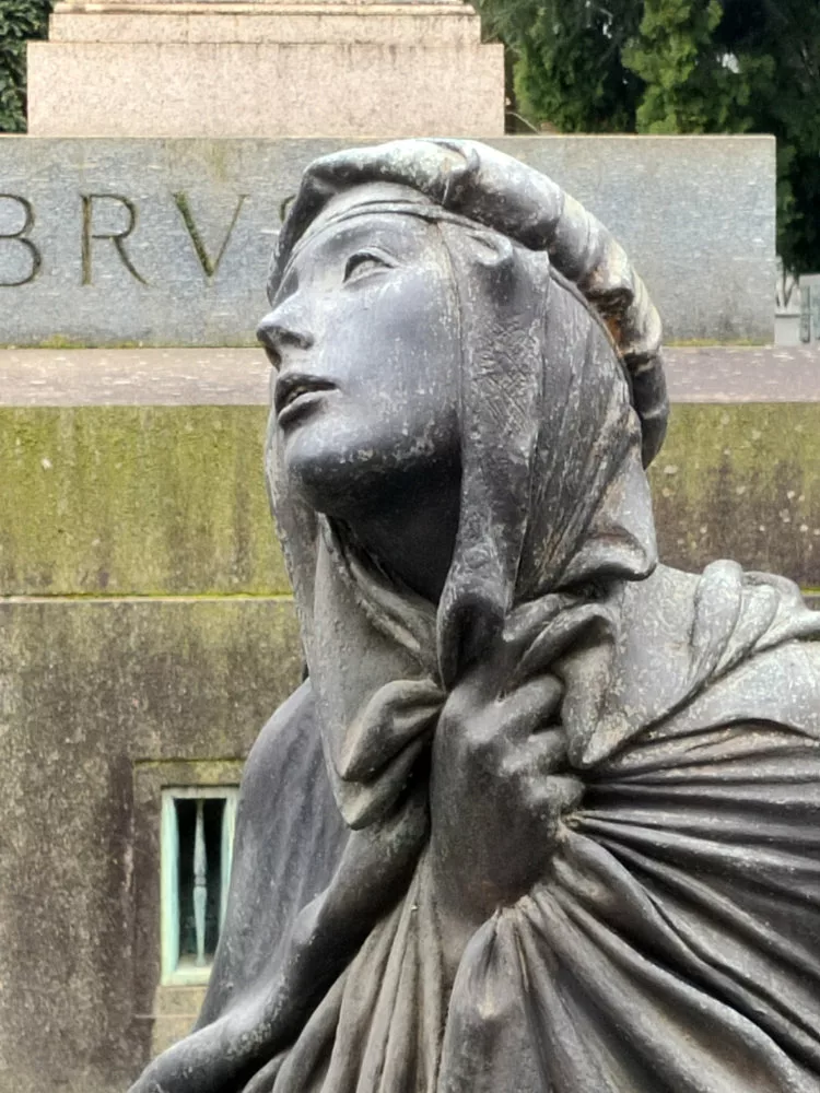 Gros plan sur une sculpture dans un cimetière représentant une femme éploré levant les yeux vers le ciel la main crispée sur son vêtement