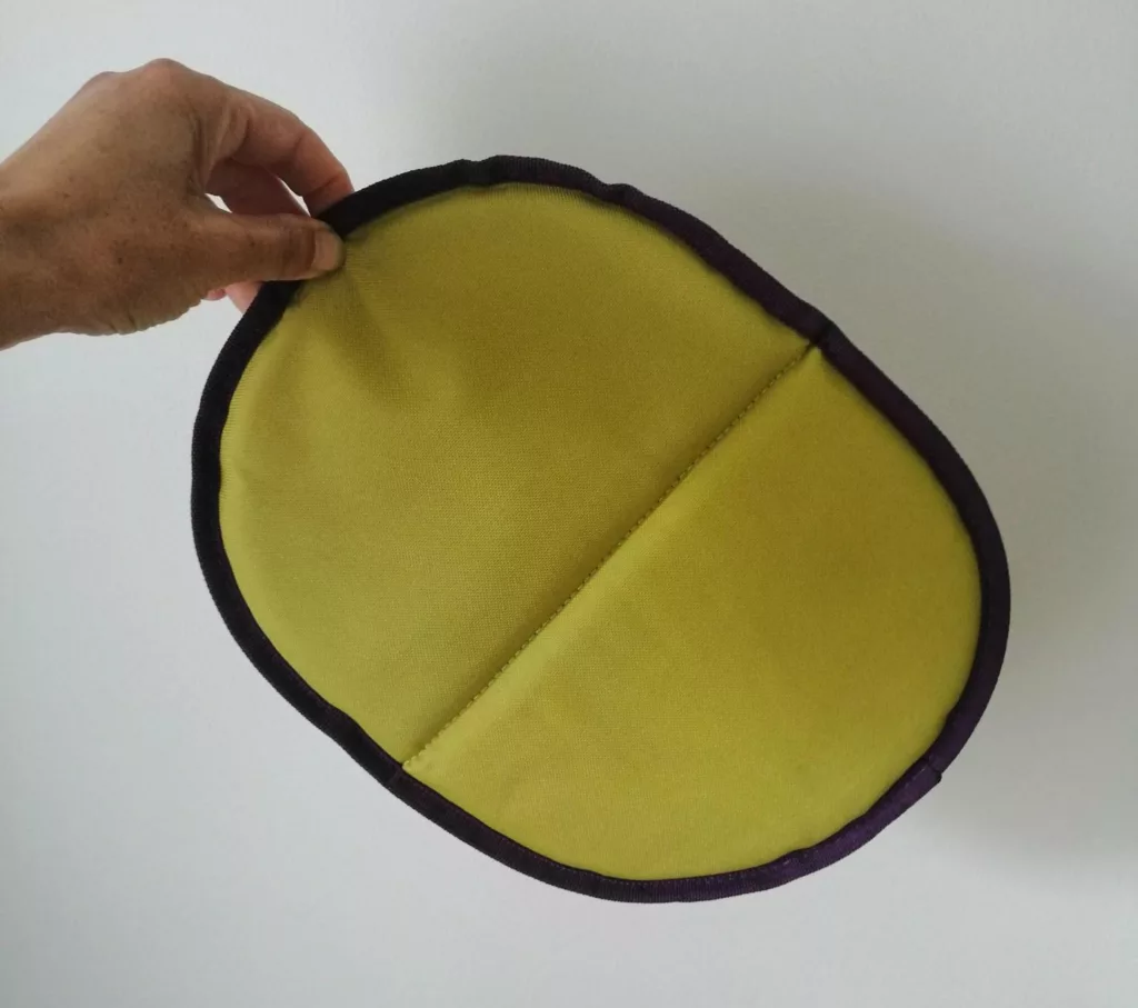 Une main tien un objet en tissu qui semble tout léger, en forme d'ovale aplatit, d'environ trente centimètres de long